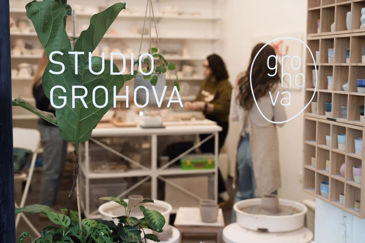 Pohled výlohou s nápisem Studio Grohova do keramické dílny s lidmi u stolu