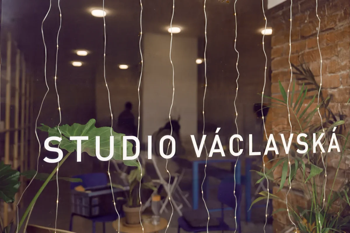 Prosklený vstup s nápisem Studio Václavská, světelným řetězem a pohledem do dílny
